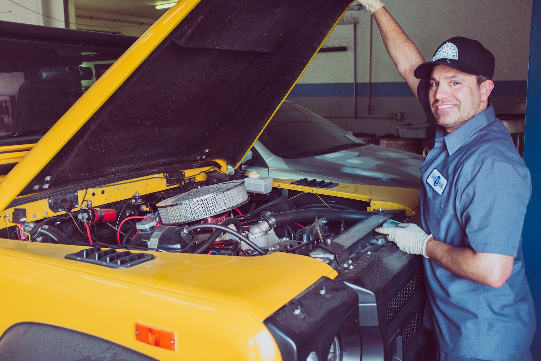 Technician checking an engine bay beside a car with its hood raised
