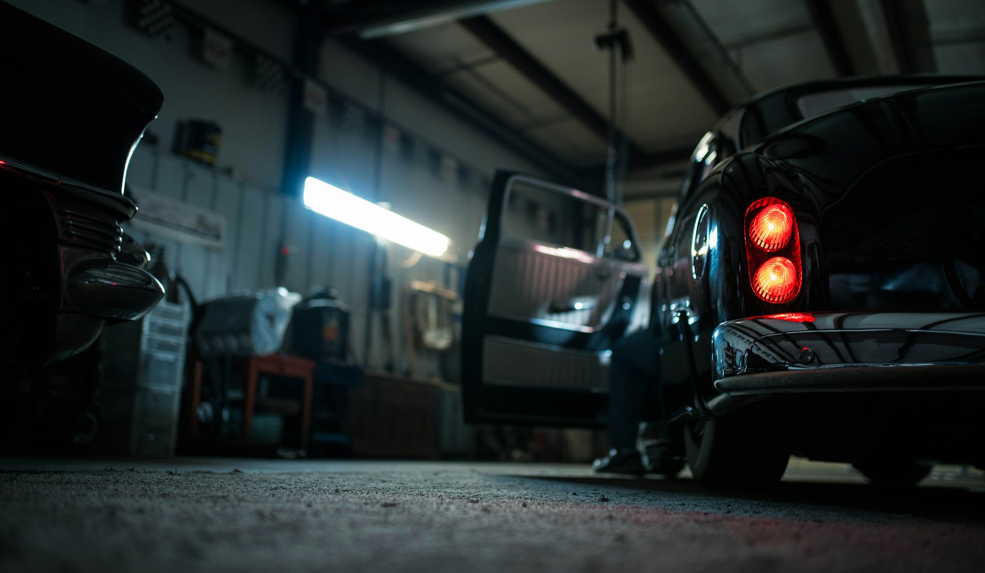 A dark workshop bay with a car and fluorescent strip lights reflecting off the floor